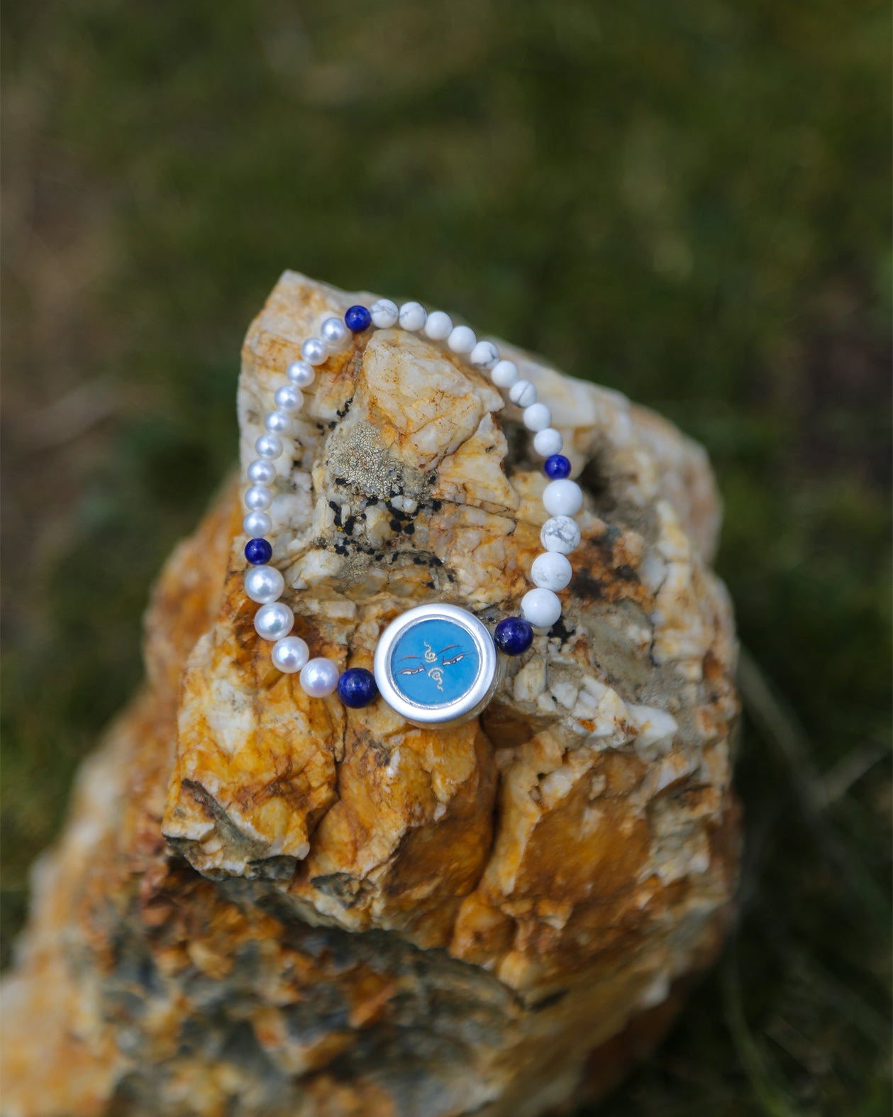 Pearl bracelet with a blue charm on a textured stone surface