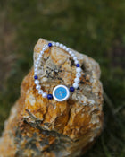 Pearl bracelet with a blue charm on a textured stone surface