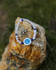 Pearl bracelet with a blue charm on a textured stone surface